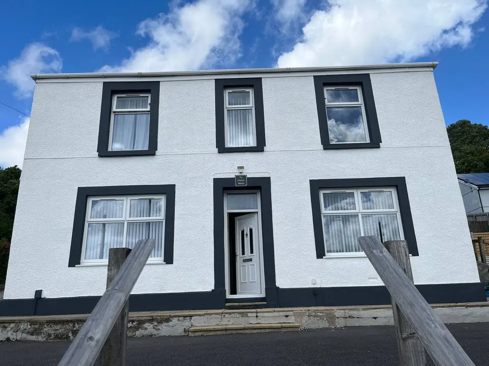 After: the same house repainted by our painters in Swansea — brilliant white masonry with deep charcoal window surrounds, door and plinth.