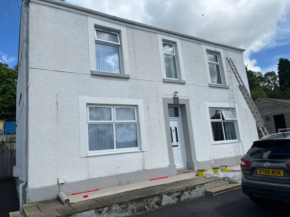 Before: a tired Swansea farmhouse with dull, patchy white render and bare grey window surrounds.